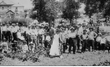 An old black-and-white photograph of Lottie Parish at the groundbreaking ceremony for the Colorado Condensed Milk Company. She is wearing a dress and using a shovel to scoop dirt, surrounded by community members.
