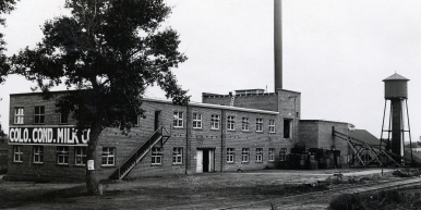 An old black-and-white photograph of the Colorado Condensed Milk Company, showing a large rectangular brick building with many windows and a small water tower.