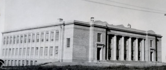 An older black and white photo of a two story brick building with multiple windows and a flat roof.