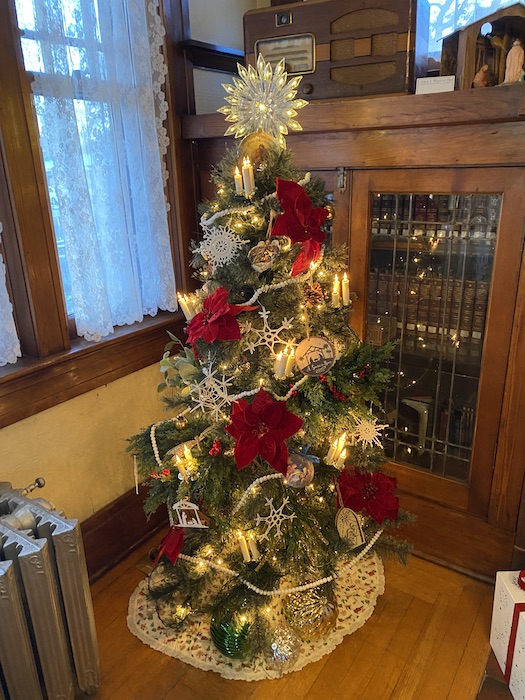 A small tree is beautifully decorated with white lights, crocheted snowflakes, red poinsettias, and a lighted star at the top.