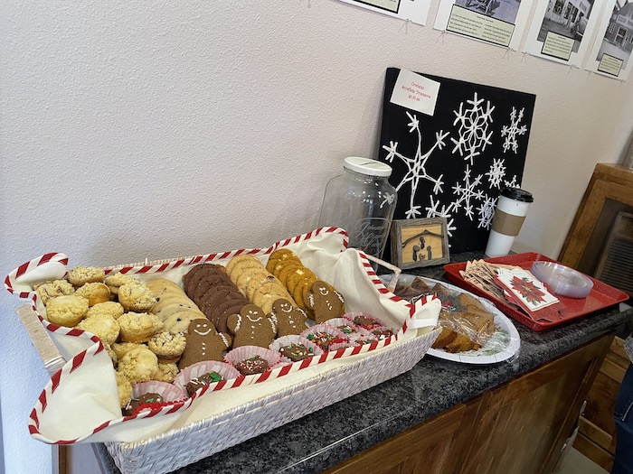 A festive display of holiday cookies including gingerbread men, fudge with sprinkles, banana bread, and muffins.
