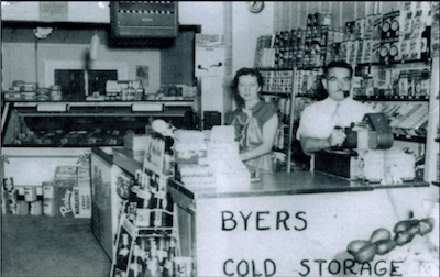 An old black and white image of a man and woman standing behind the register counter insider a store.