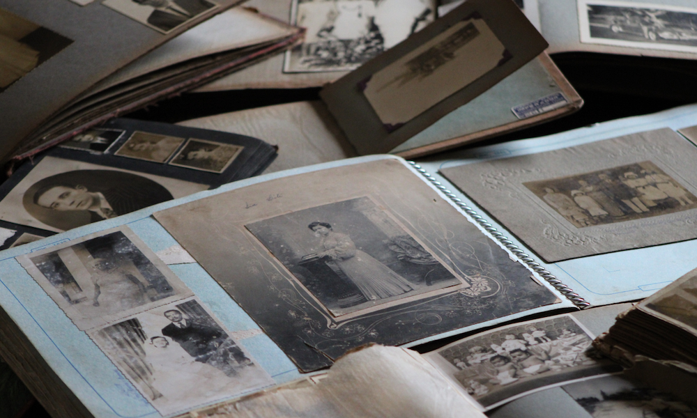 A photo showing old black and white photos in an album and spread across a table.