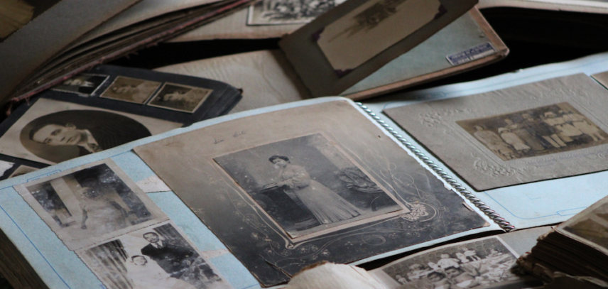 A photo showing old black and white photos in an album and spread across a table.